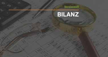 Titelbild zum Thema Bilanz: Auf einem Zahlenblatt liegen ein Taschenrechner, ein Stift und eine Brille; rechts ist eine große Lupe zu sehen. Oben steht „Vereinswelt“, mittig der große Schriftzug „BILANZ“.