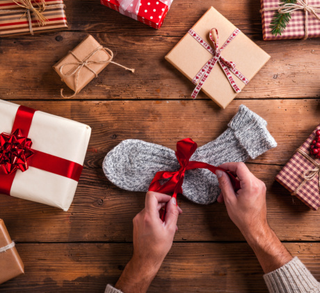 Geschenke auf einem Holztisch. Zwei Hände binden eine Schleife um eine Socke.