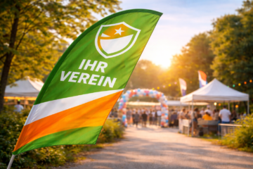 Nahaufnahme einer im Wind wehenden Beachflag in Grün und Orange mit dem Schriftzug ‚IHR VEREIN‘; im unscharfen Hintergrund ein Eventgelände mit Zelten und Lichterketten.