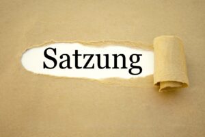 Braunes Papier, aufgerissen, zeigt das Wort "Satzung" in schwarzer Schrift.