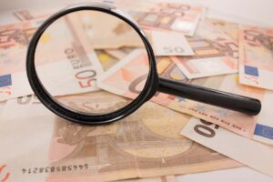 Lupe vergrößert Euro-Geldscheine auf einem Tisch.