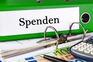 Grüner Ordner mit „Spenden“ als Label, daneben Euro-Geldscheine und ein Taschenrechner.